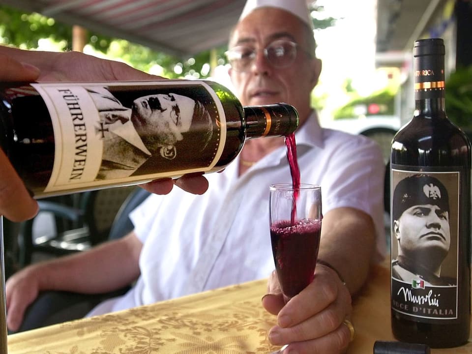 Ein Mann verkostet Wein aus Flaschen mit Hitler und Mussolini-Ettikett.
