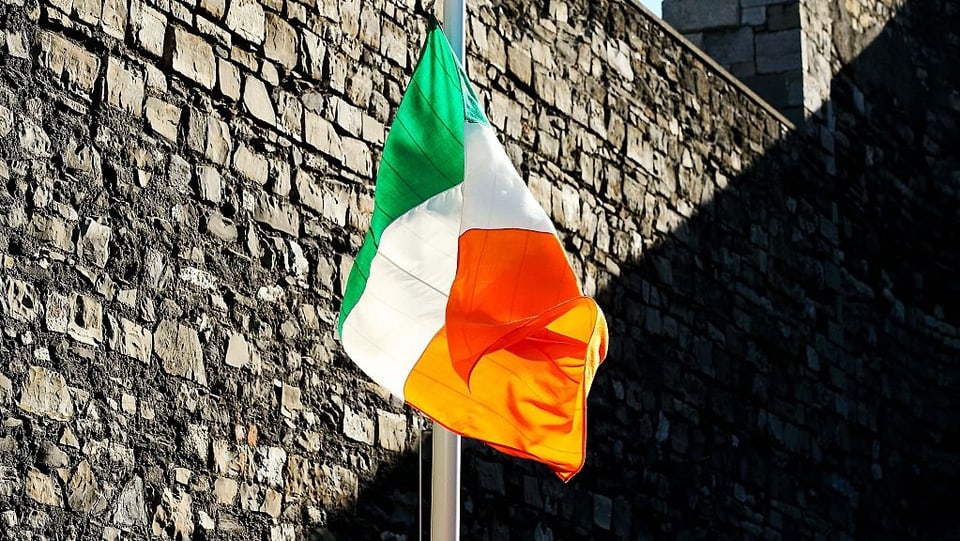 Eine irische Flagge vor einer Steinmauer.