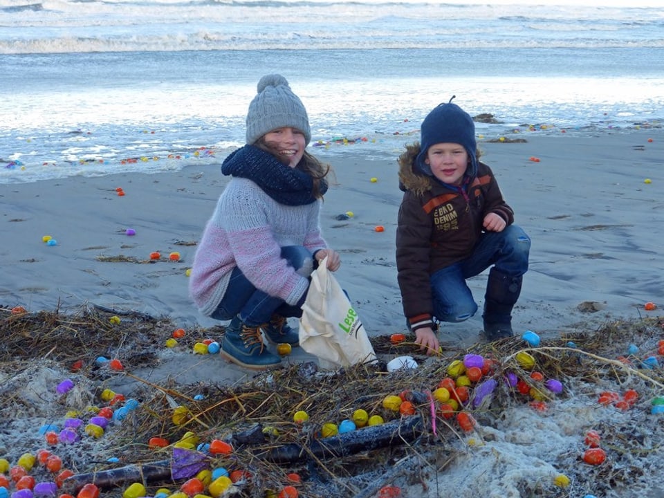 Kinder sammeln farbige Überraschungseier an Strand.