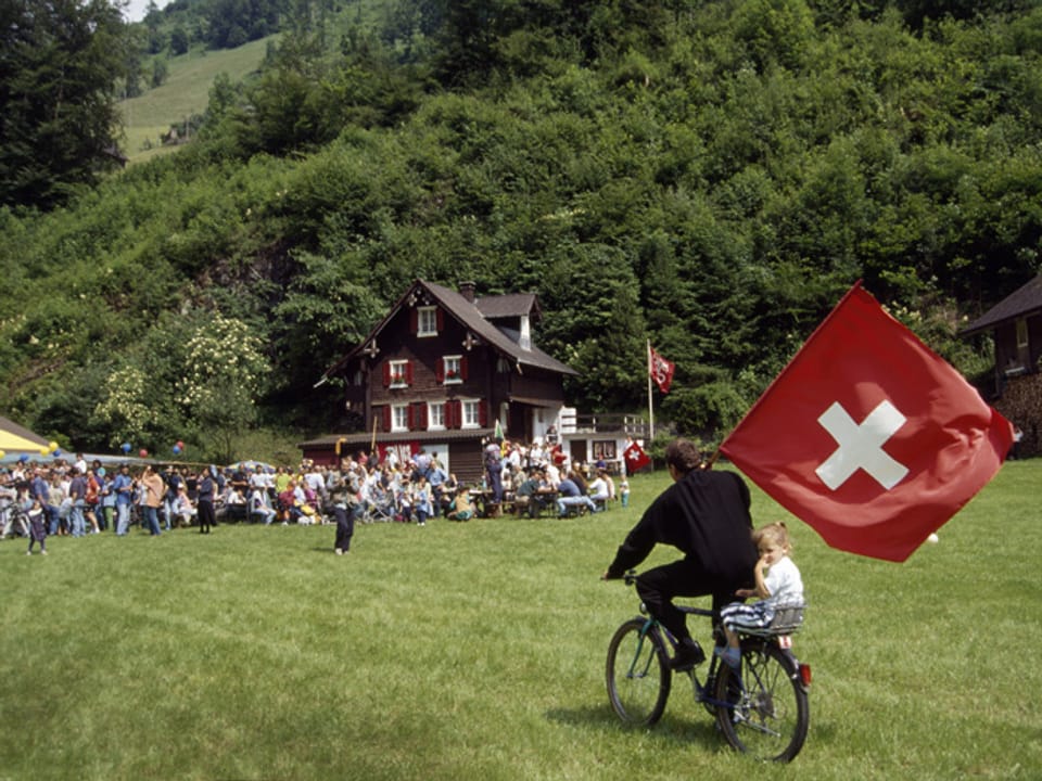 Mann auf Fahrrad mit Schweizer Fahne und Kind auf Gepäckträger.