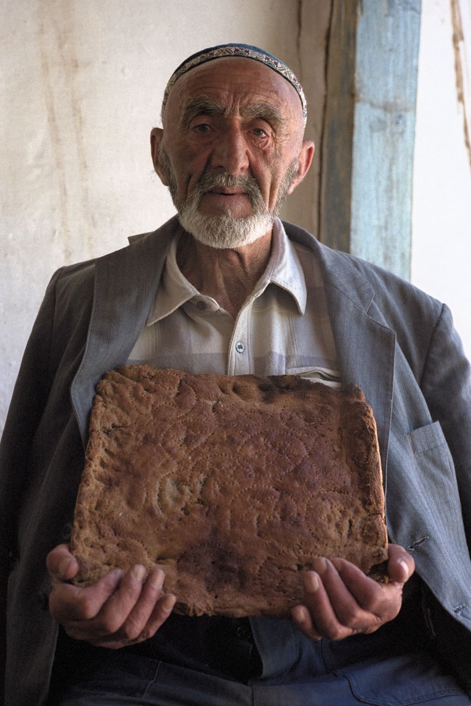 Ein älterer Mann hält einen grossen Brotlaib, der mit Mustern verziert ist.
