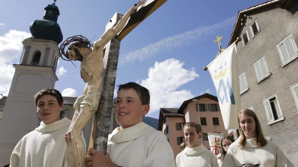 Kinder in Ministrantentracht tragen Kreuz durch ein Dorf.