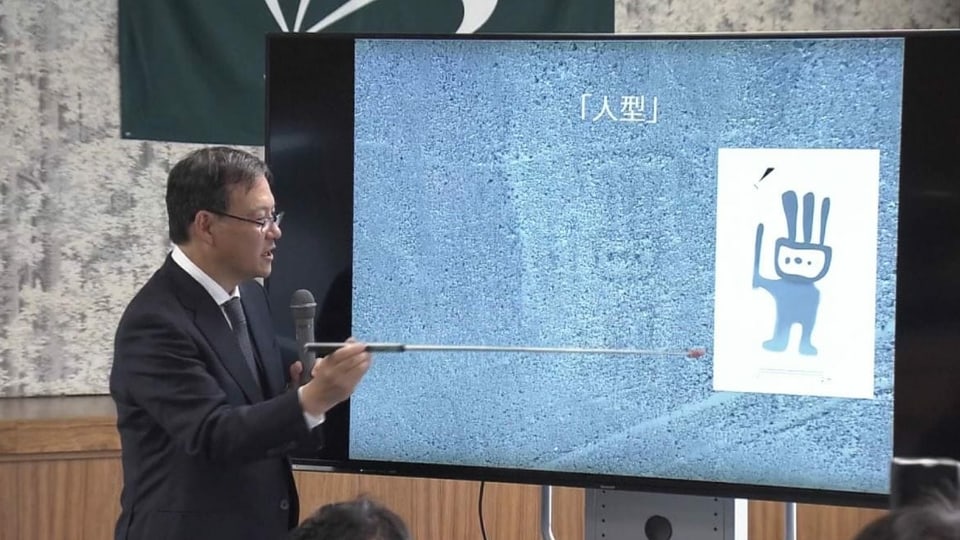 Japanischer Forscher zeigt auf einer Leinwand die vermeintliche Figur.