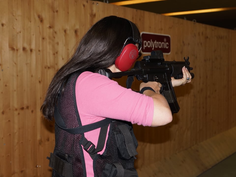 Eine Frau mit dunklen langen Haaren zielt mit einer Maschinenpistole auf eine Zielscheibe.