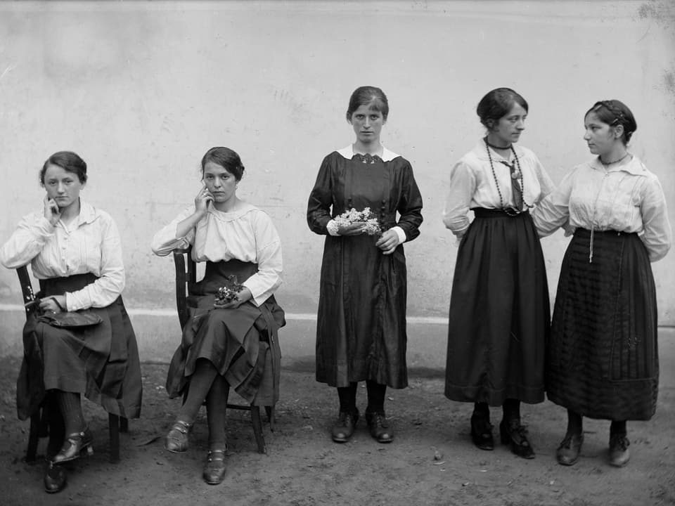 Fünf festliich gekleidete Frauen – zwei auf Stühlen sitzen, drei stehend.