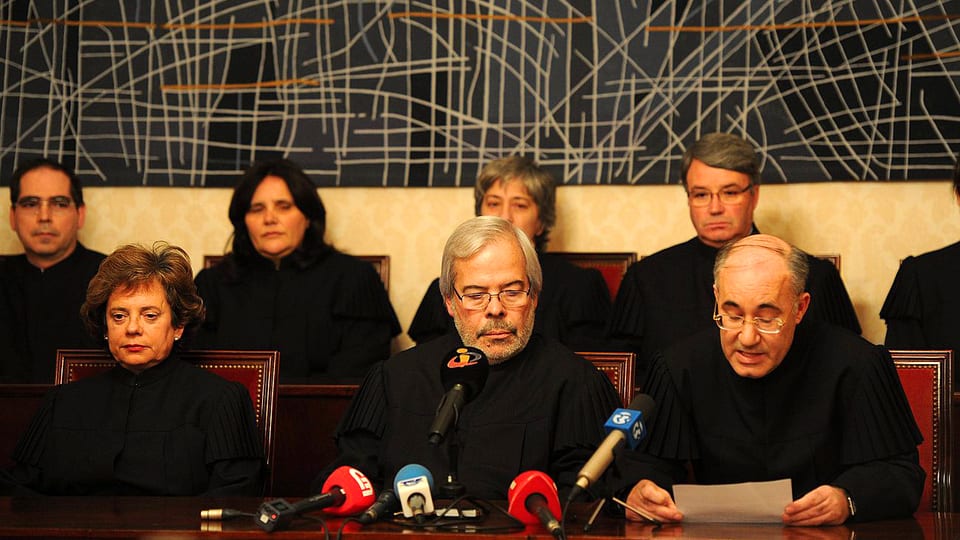 Sitzende Richter in schwarzen Roben, im Vordergrund stehen Mikrofone.