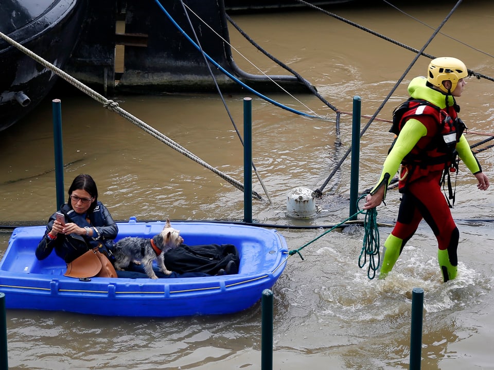 Ein Feuerwehrmann mit Helm zieht eine Frau in einem blauen Schlauchboot ans Ufer.