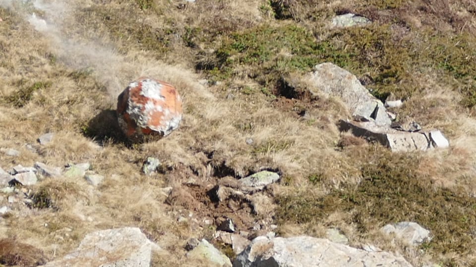 Ein künstlicher Stein rollt mit hoher Geschwindigkeit einen mit Steinen durchsetzen Grashang herunter.