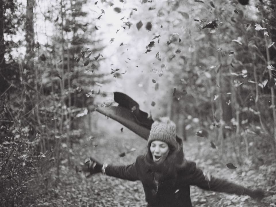 Ein Mädchen wirft im Wald Herbstlaub durch die Luft und jubelt (Schwarz-Weiss-Bild)