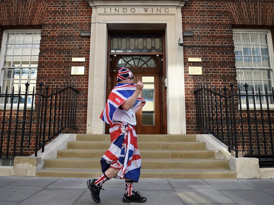 Eine Person in der britischen Flagge eingehüllt geht vor einem Eingang.