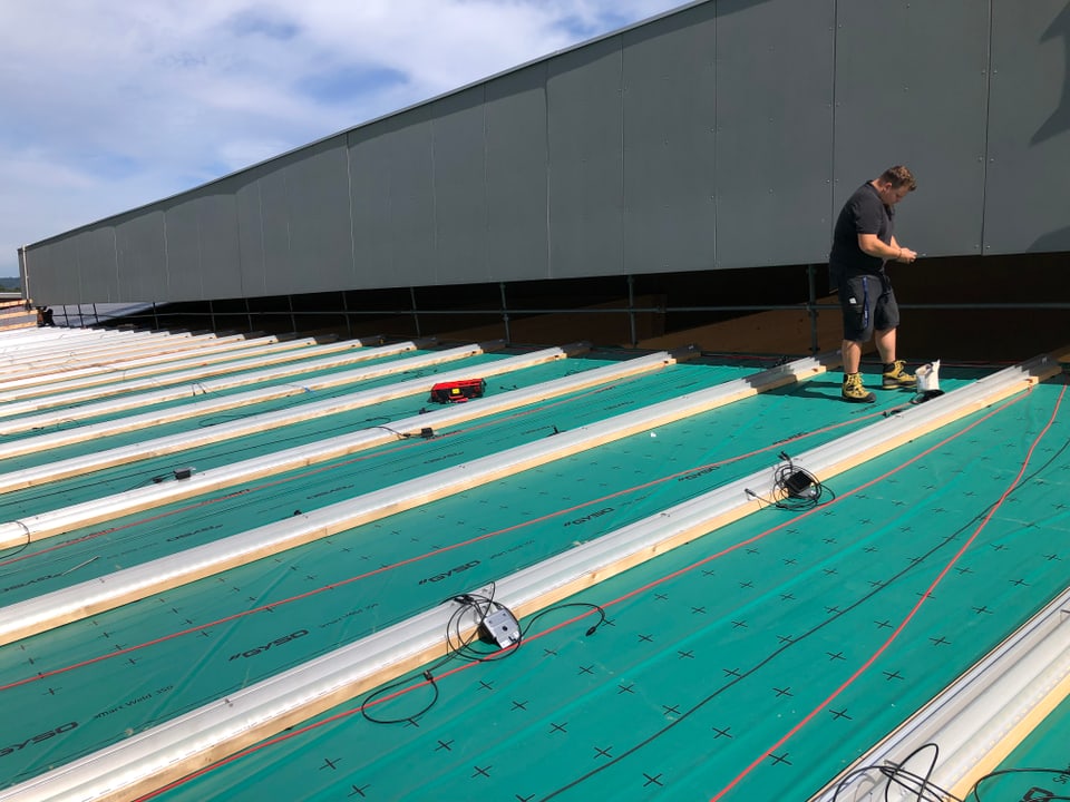 Ein Facharbeiter erledigt die letzten Schritte an einer neuen Solaranlage auf dem Dach einer Sägerei.