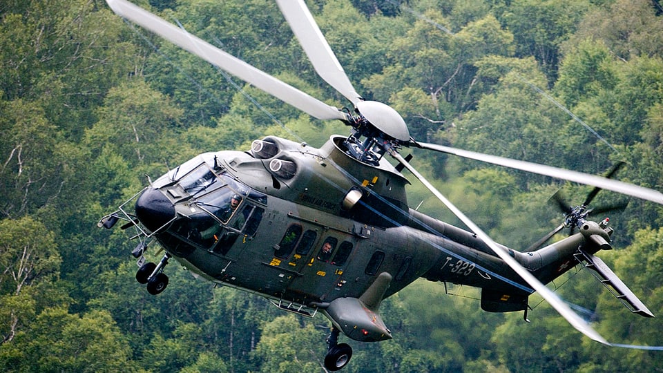 Fliegender Super-Puma-Helikopter der Schweizer Armee über einem Waldgebiet.