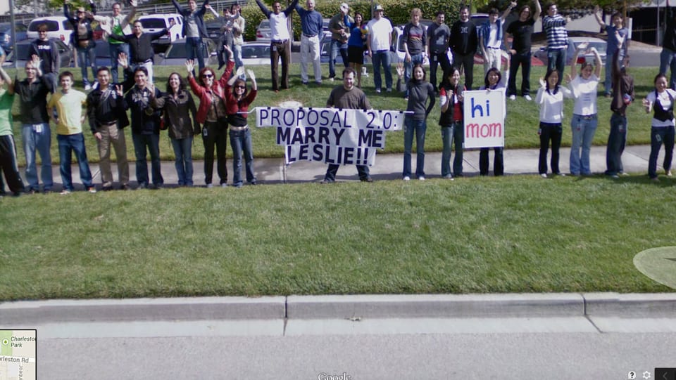 Viele Google Angestellte am Strassenrand, einer hält ein Transparent, auf dem steht: "MARRY ME, LESLIE!"