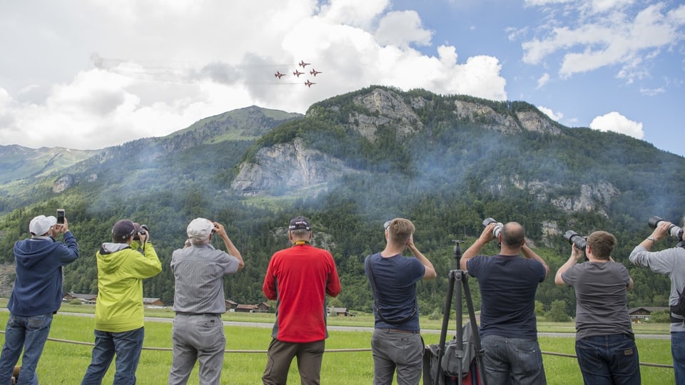 Menschen mit Fotokameras stehen vor Bergen und fotografieren die Patrouille Suisse. 