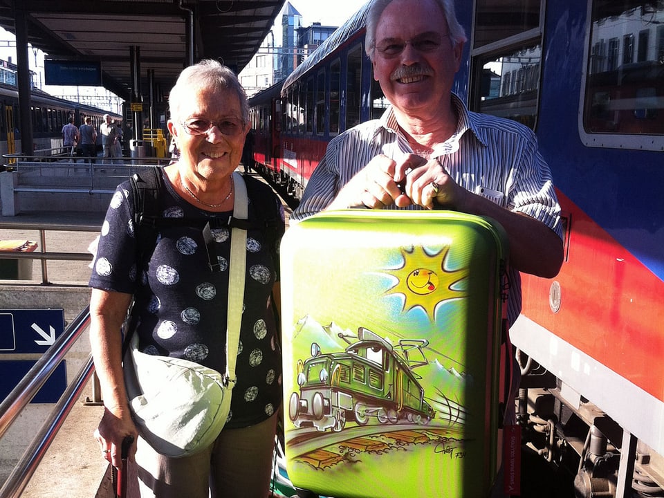 Ein älteres Paar steht mit Koffer neben dem Zug auf dem Perron.