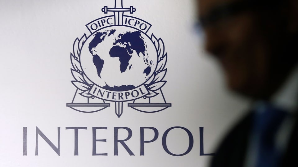 Interpol-Logo, der Schatten eines Mannes davor.