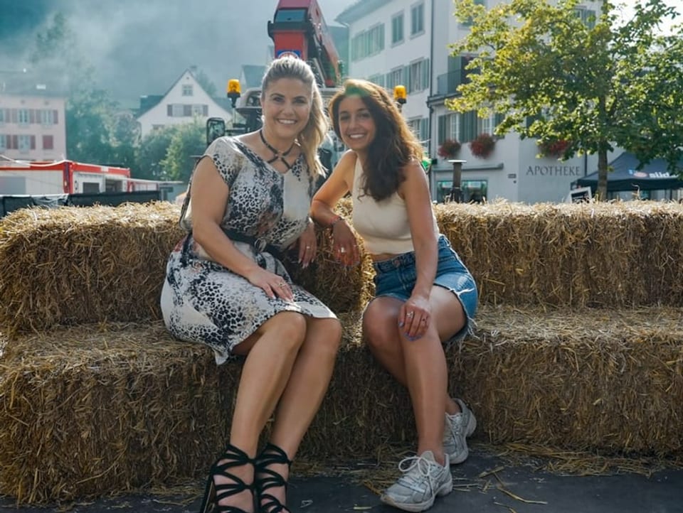 Beatrice Egli und Céline Werdelis sitzen auf Strohballen vor einem Traktor