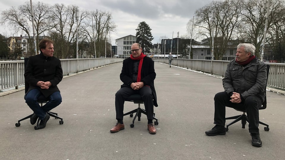 Drei Herren sitzen auf Bürostühlen auf der Kreuzackerbrücke in Solothurn und reden miteinander.