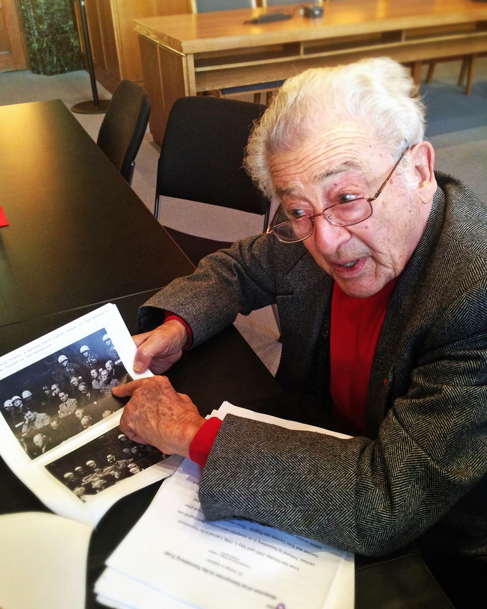 Weisshaariger Mann zeigt schwarz-weiss Bilder der Nürnberger Prozesse.