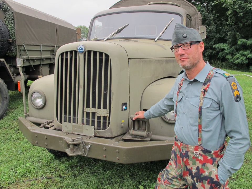Hildinger trägt eine Originaluniform und steht vor seinem Lastwagen.