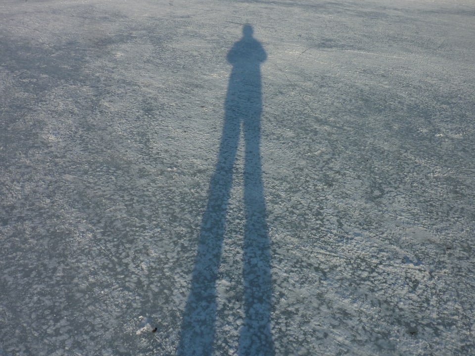 Der langgezogene Schatten eines Kindes auf der Eisdecke eines Sees.
