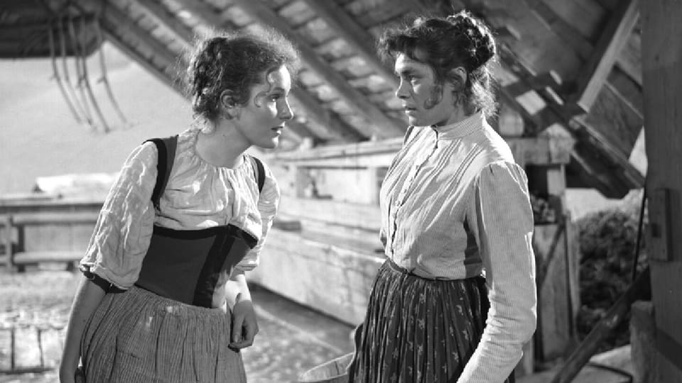 Zwei Frauen in Bauerngewand stehen im Heustock und starren sich gegenseitig an.