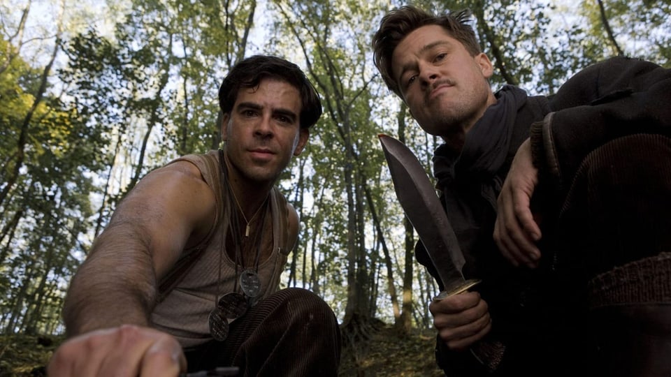 Brad Pitt and Eli Roth look at the camera.