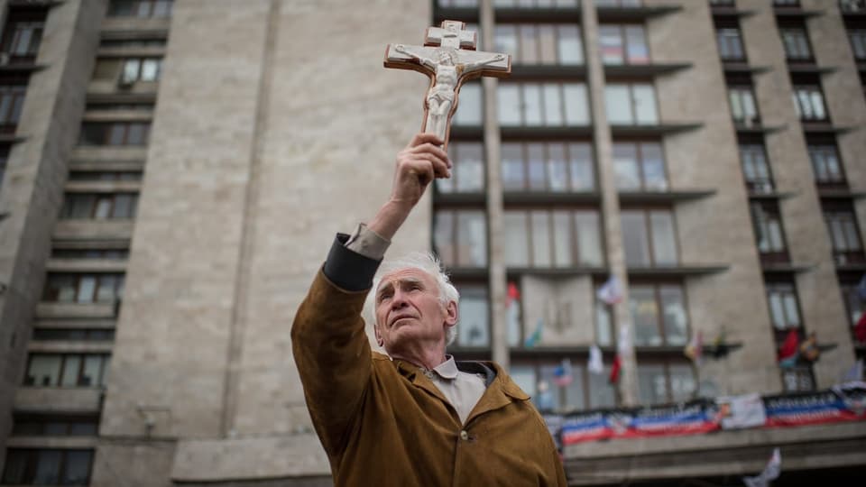 Mann hält ein Kreuz in die Luft.