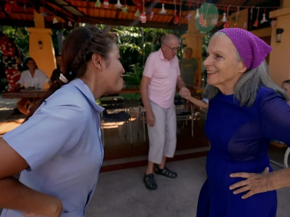 Eine thailändische Frau in blauer Uniform tanzt mit einer älteren Frau.