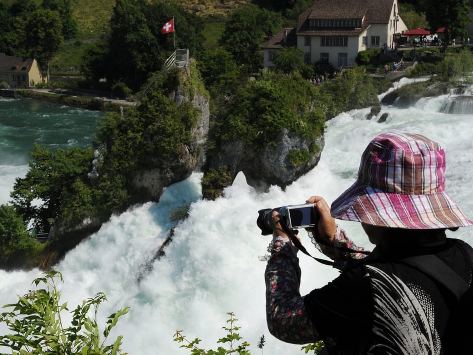 Zu sehen ist eine Touristin, die den tosenden Rheinfall in Schaffhausen fotografiert.