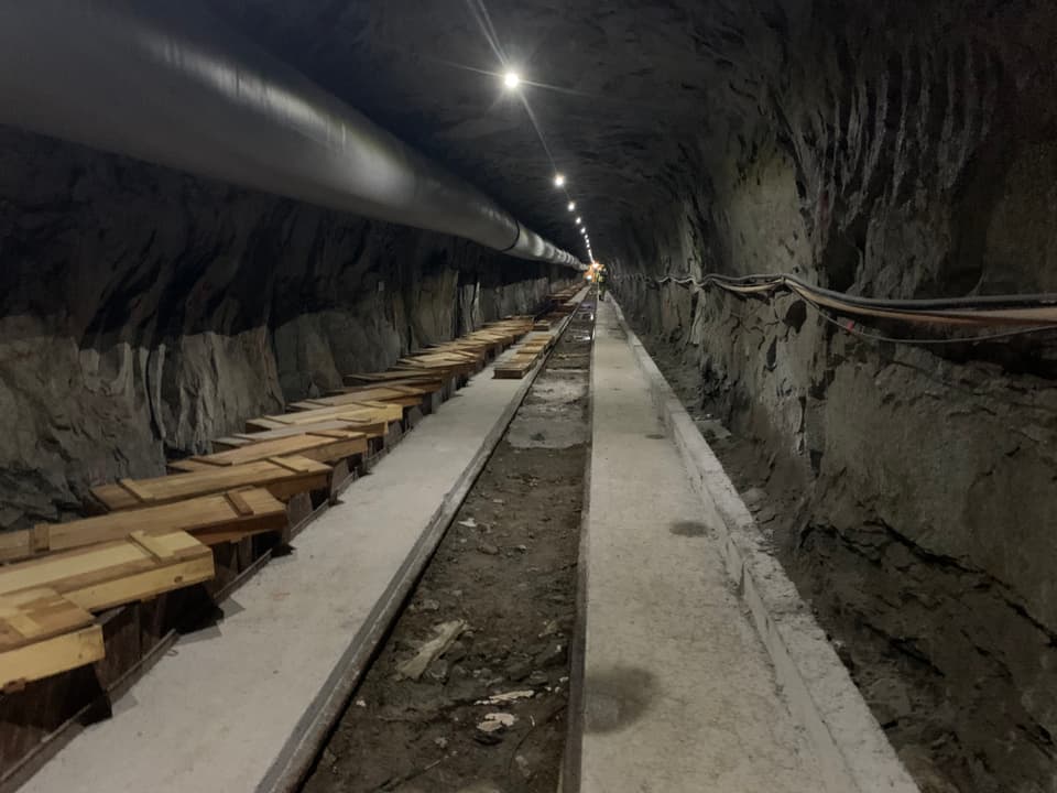 Langer Tunnel, dickes Rohr an der Decke, Holzscheite links am Rand