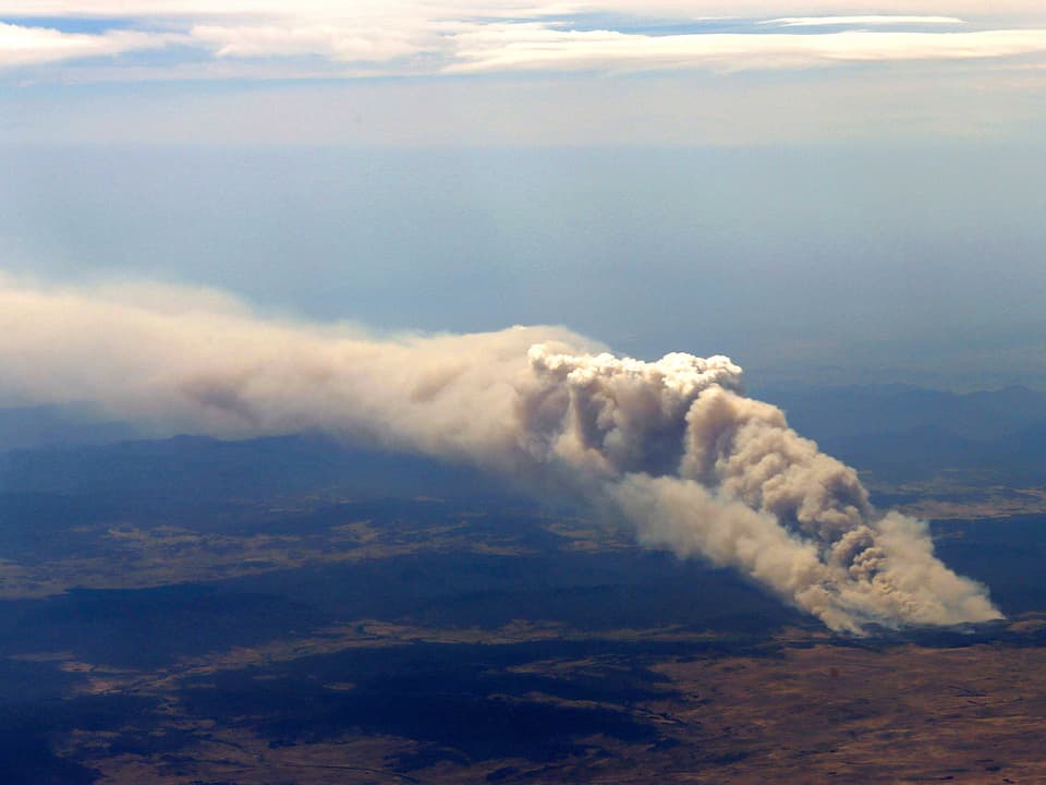 Sicht aus einem Passagierflugzeug auf eine weit in den blauen Himmel über Cooma aufsteigende Rauchsäule.