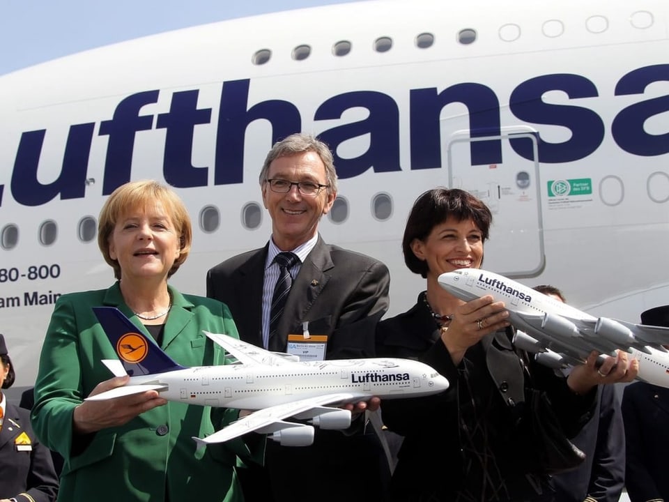 Merkel und Leuthard halten Flugzeugmodelle in die Höhe.