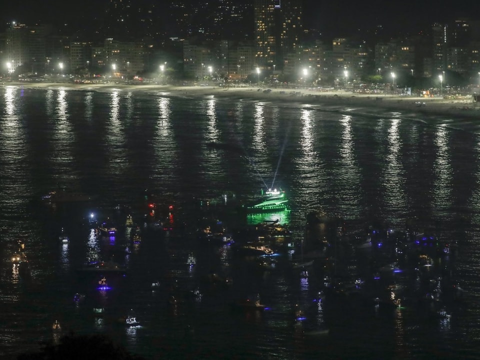 Nachtansicht auf beleuchtete Boote vor einer belebten Stadt am Meer