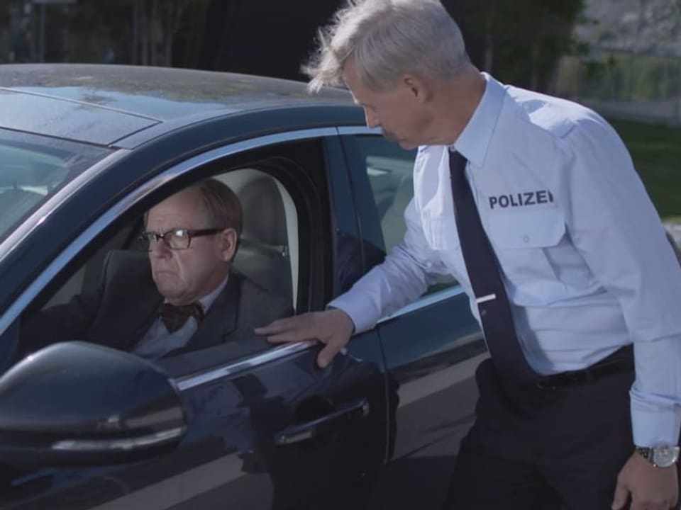 Ein Mann mit Brille sitzt in einem schwarzen Auto, die Scheibe heruntergelassen. Ein Polizist spricht mit dem Fahrer..