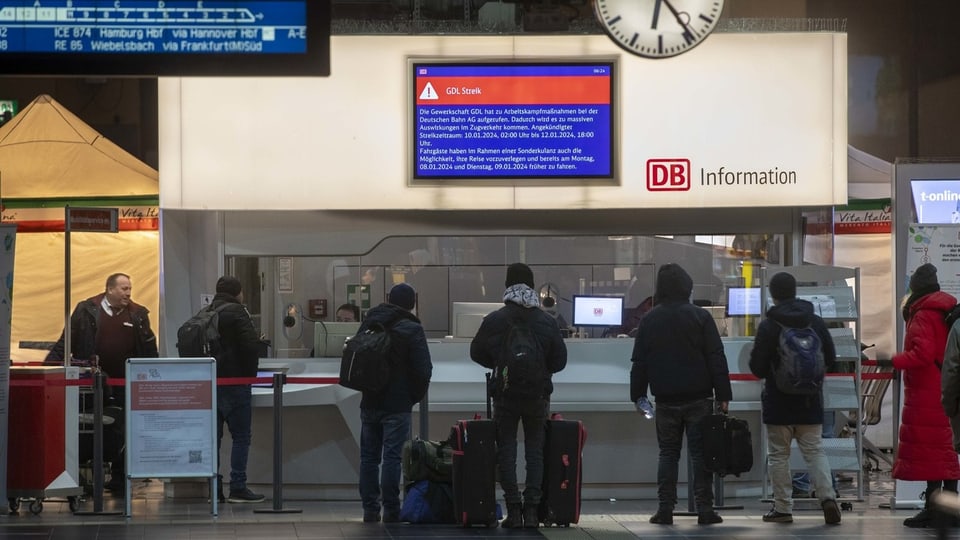 Reisende stehend vor einem Infoschalter der Deutschen Bahn