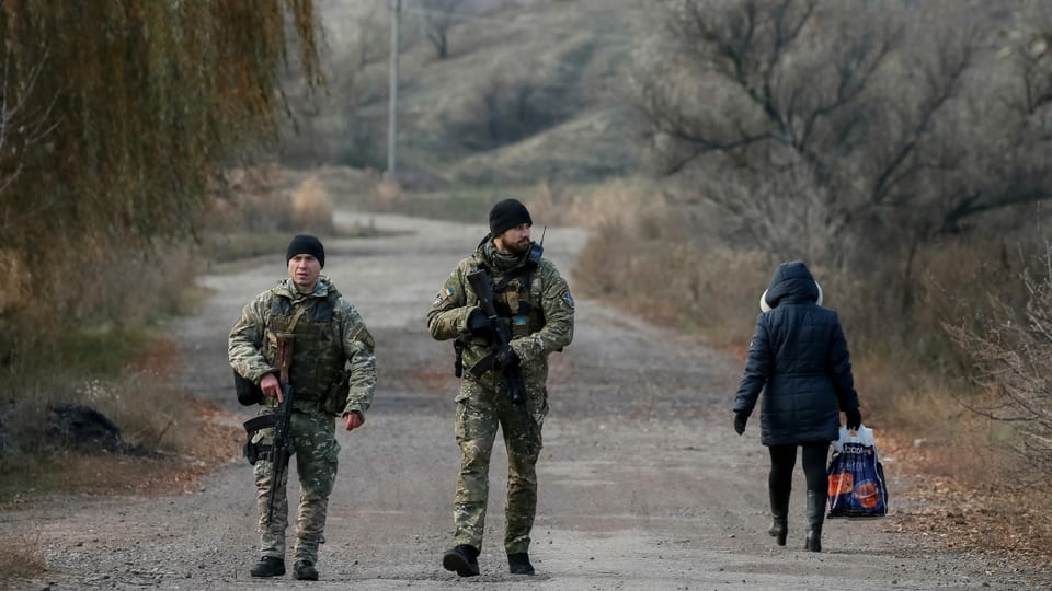 Soldaten patrrouillieren auf einer Strasse im Donbass, eine Zivilistin geht vorbei.