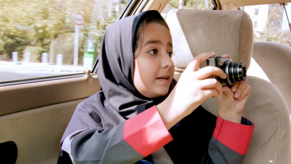 Ein Mädchen mit einem Kopftuch sitzt im Taxi und fotografiert.