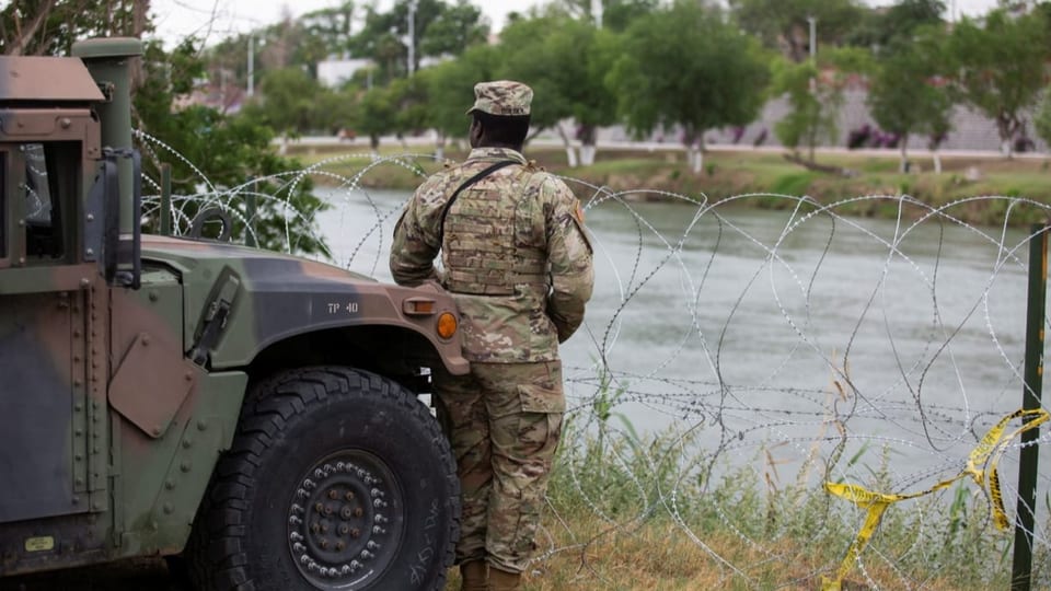 Ein Grenzschutzwächter steht neben einem Stacheldraht bei einer Grenze.