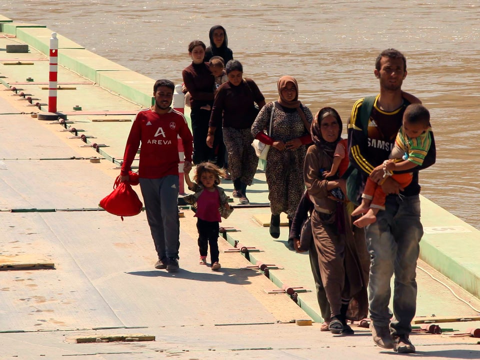 Männer und Frauen mit Kindern ohne Gepäck schreiten über eine Brücke.
