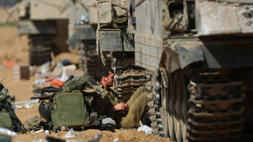 Soldat sitzt neben Militärfahrzeugen am Boden und ruht sich aus.