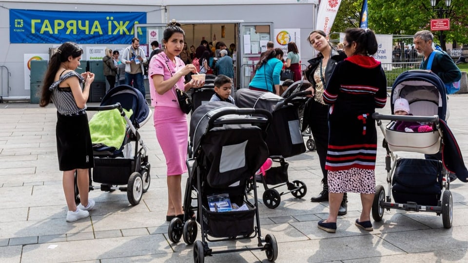 Frauen mit Kinderwagen vor Zelt