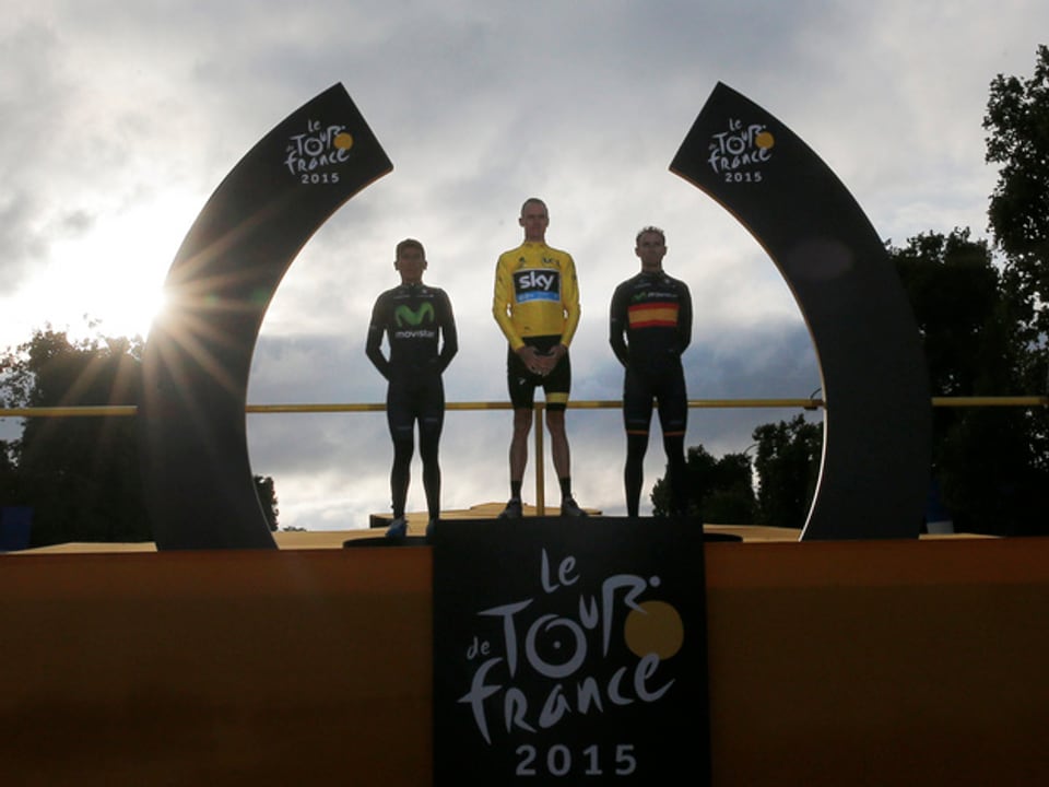 Chris Froome steht zusammen mit Nairo Quintana und Alejandro Valverde auf dem Podium, im Hintergrund geht die Sonne über Paris langsam unter.