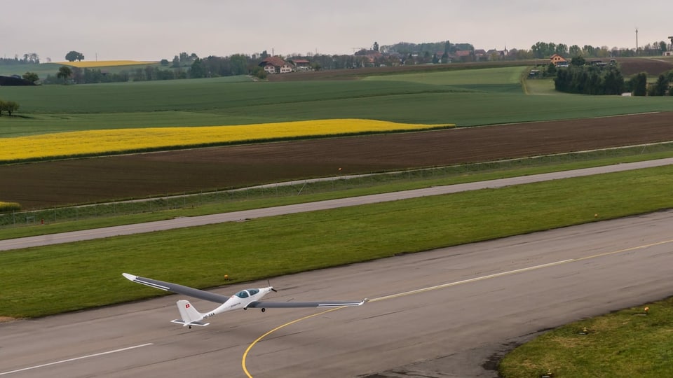 Ein Flugzeug mit Solarpanels auf den Flügeln beim Start auf einem ländlichen Schweizer Flughafen.