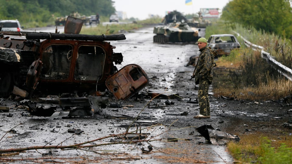 Ein ukrainischer Soldat steht neben einem zertörten Panzer