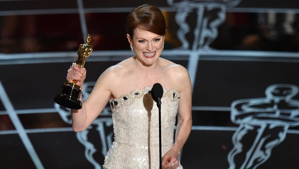 Julianne Moore hält einen Oscar in der Hand, lächelt und spricht in ein Mikrofon.