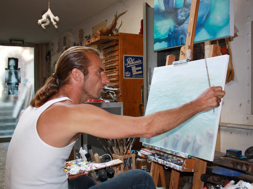 Ein Mann sitzt vor einer Leinwand und malt ein Bild.