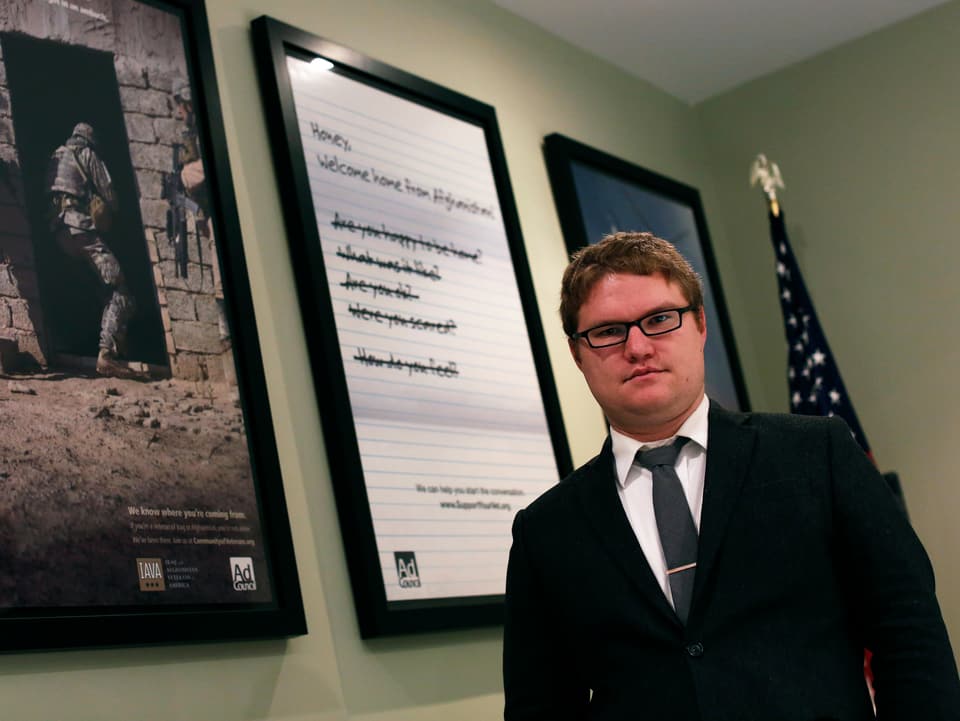 Ein Mann steht in einem Büro, hinter ihm hängen drei Bilder an der Wand.