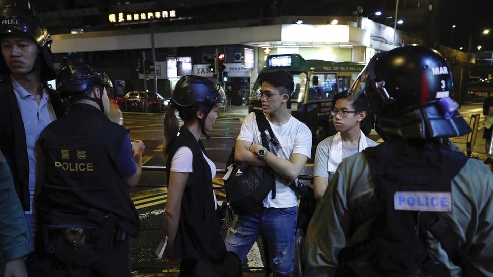Zwei junge Männer, Zivilisten, neben einigen Polizeibeamten in Hongkong