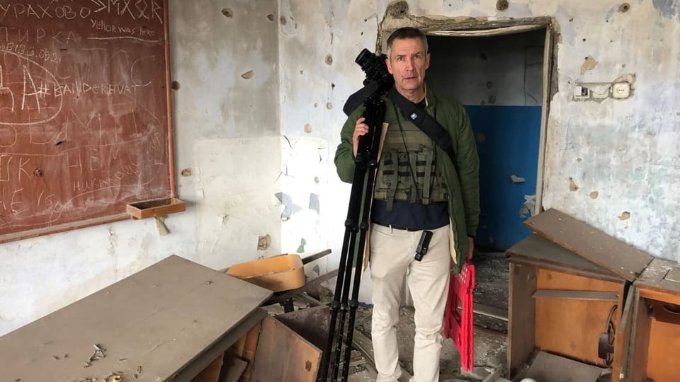 The man with the camera and tripod in his hand, stands in a photo room and looks at the camera.